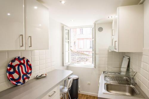 une cuisine avec des armoires blanches, un évier et une fenêtre dans l'établissement Les Cordeliers, à deux pas de capitole, à Toulouse