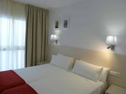 a bedroom with a bed with white sheets and a window at Apartamentos Patagonia Sur in Cádiz