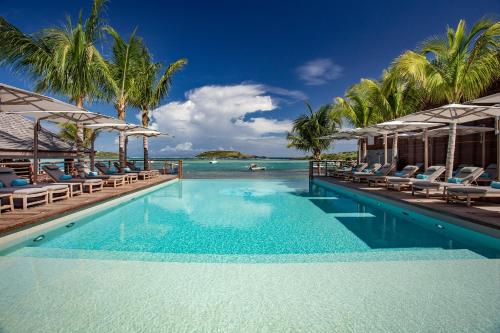 a pool with chairs and the ocean in the background at Le Barthélemy Hotel & Spa in Gustavia