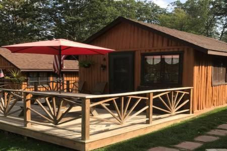 a cabin with a deck with a red umbrella at Clear Lake Resort in West Branch