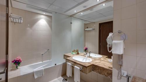 a bathroom with a sink and a tub and a mirror at Center Hotel Sharjah in Sharjah