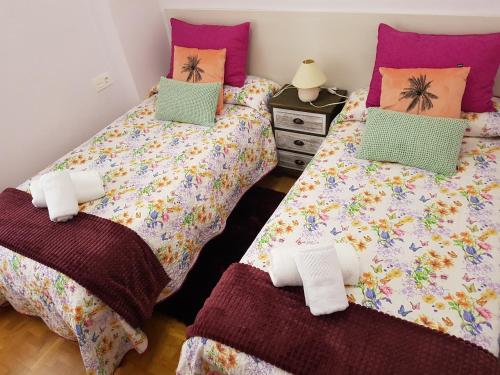 two beds in a bedroom with purple and green pillows at Apartamento Manzanera in Logroño