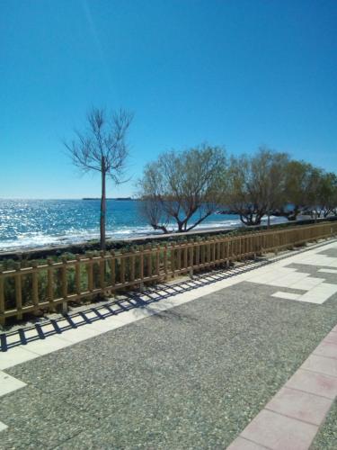 a wooden fence next to the ocean with trees at Comfy Apartment near the Sea in Ierápetra