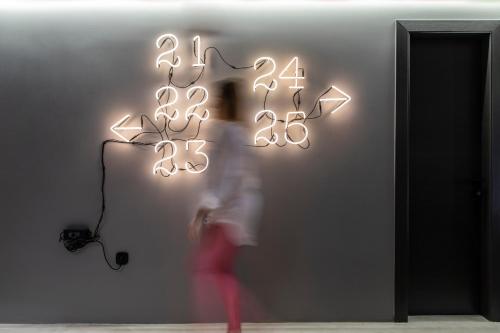 a person walking past a neon sign with numbers on a wall at 14 Reasons Why Hotel Athens in Athens