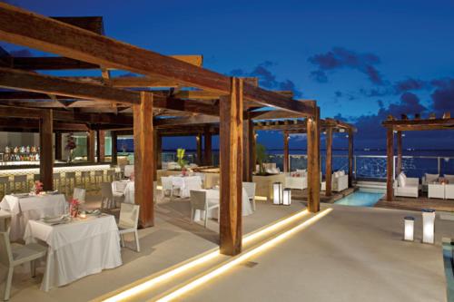 un restaurante con mesas y sillas blancas y el océano en Secrets The Vine Cancun - All Inclusive Adults Only, en Cancún