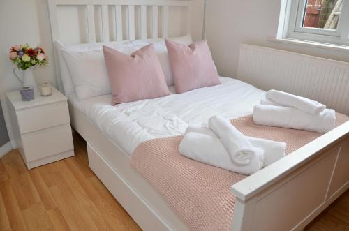 a white bed with pink pillows and towels on it at Croydon apartment with parking in London