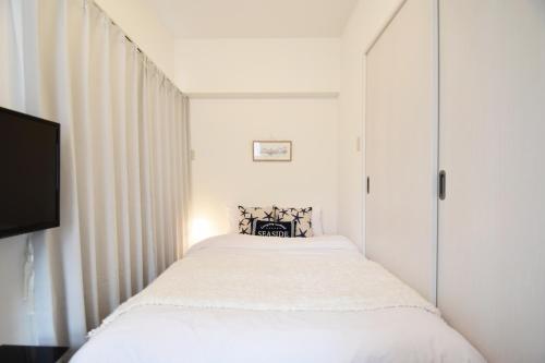 a white bedroom with a bed and a tv at Enjoymaru 202 in Naha