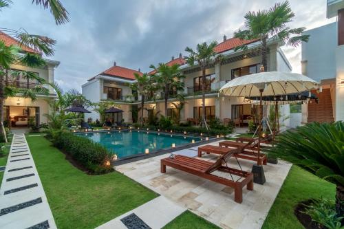 a resort pool with benches and an umbrella at Puri Uma Ratu by RPM in Seminyak