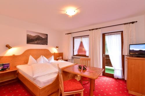 a bedroom with a bed and a table and a television at Landhaus Almrausch in Mittelberg