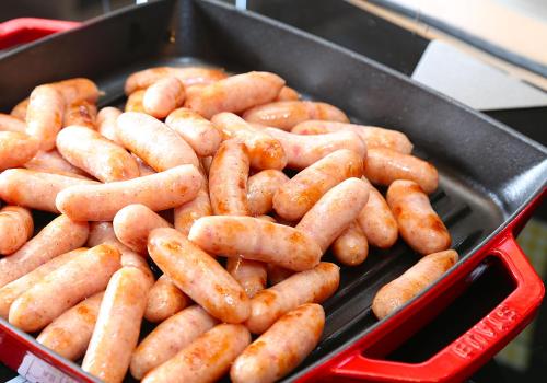 a bunch of sausages are cooking in a pan at Daiwa Roynet Hotel Hiroshima-ekimae in Hiroshima