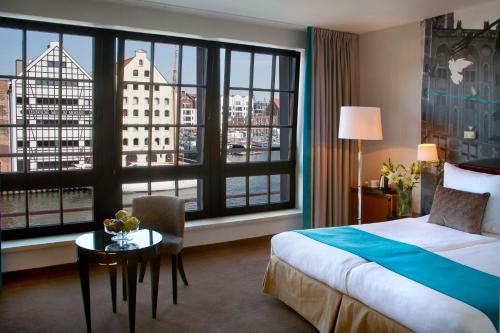 a hotel room with a bed and a table and windows at Hotel Hanza in Gdańsk