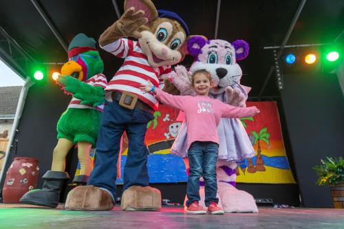 a little girl standing next to mascots on a stage at Camping Officiel Siblu Domaine de Dugny in Onzain