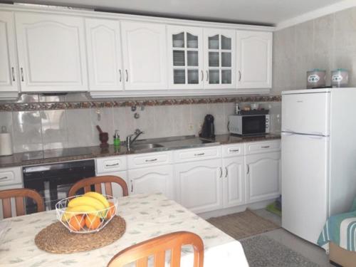 una cocina con armarios blancos y una mesa con un bol de fruta en Casa BeijoMar, en Nazaré