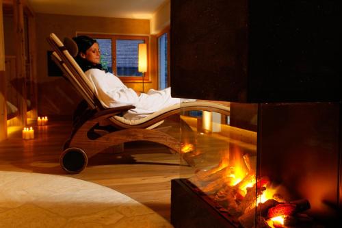 a woman sitting in a chair next to a fireplace at Hotel Ratschingserhof in Racines