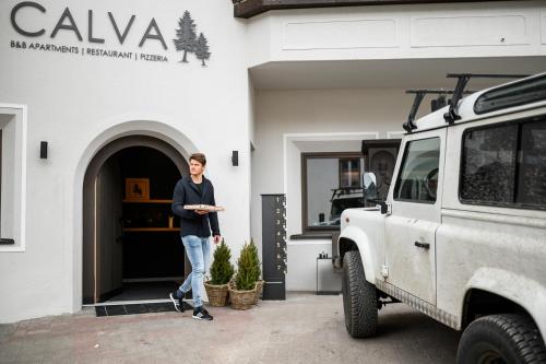 a man standing in front of a building next to a car at Calva B&B Apartments in Malles Venosta