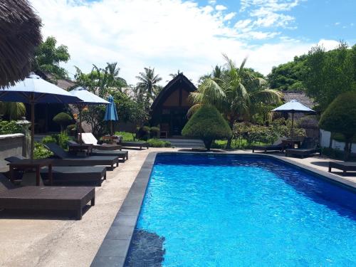 a pool at a resort with lounge chairs and umbrellas at Sandy Beach Bungalows in Gili Islands