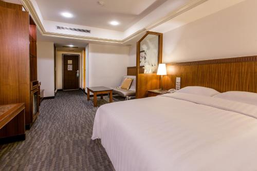 a hotel room with a large white bed and a chair at Hub Hotel Ximen-inn Kunming in Taipei