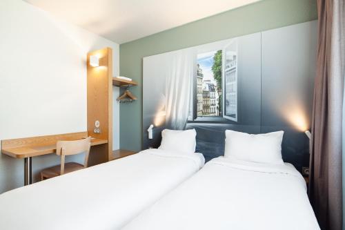 two beds in a room with a desk and a window at B&B HOTEL Paris Le Bourget in Le Bourget
