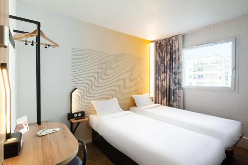 una camera d'albergo con due letti, una scrivania e una finestra di B&B HOTEL Paris Saint-Denis Pleyel a Saint-Denis
