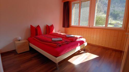 a bedroom with a bed with red sheets and a window at Ufem Egg Ferienwohnungen in Innertkirchen
