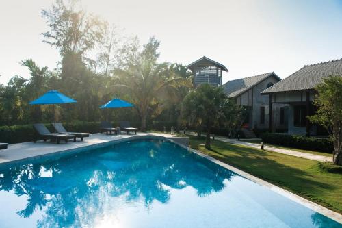 a swimming pool with chairs and umbrellas next to a house at Na Vela Village - Adults Only Hotel in Ko Lanta