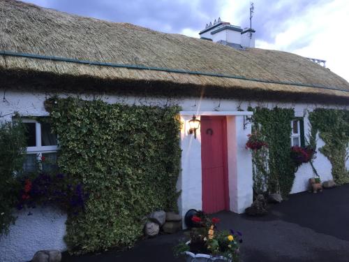 um chalé com um telhado de palha e uma porta vermelha em Teresas Cottage em Donegal
