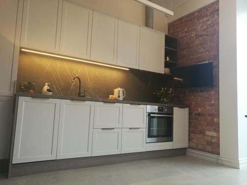 a kitchen with white cabinets and a brick wall at Apartamentai Veiveriu 16 in Kaunas