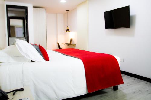 a bedroom with a bed with a red blanket and a flat screen tv at Hotel WLH Bogota - White Lighthouse in Bogotá