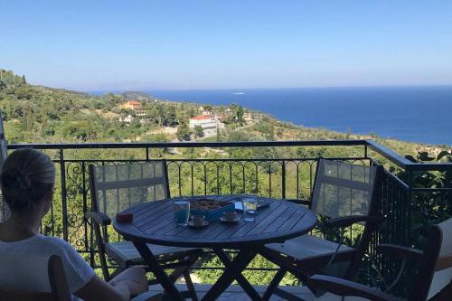 a woman sitting at a table on a balcony overlooking the ocean at Aegean Breeze Mansion in Kymi