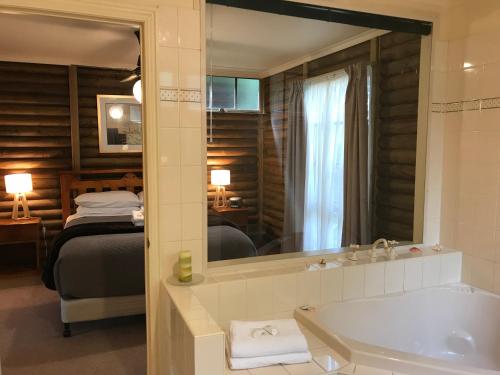 a bathroom with a tub and a bed and a mirror at Ti-Tree Village in Ocean Grove