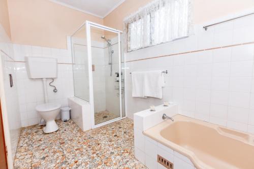 a white bathroom with a tub and a toilet at Best Central House - SLEEPS 12 !! in Wagga Wagga