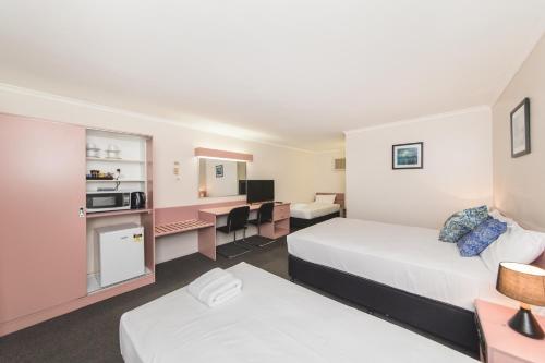 a hotel room with two beds and a desk at Metro Motel Rockhampton in Rockhampton