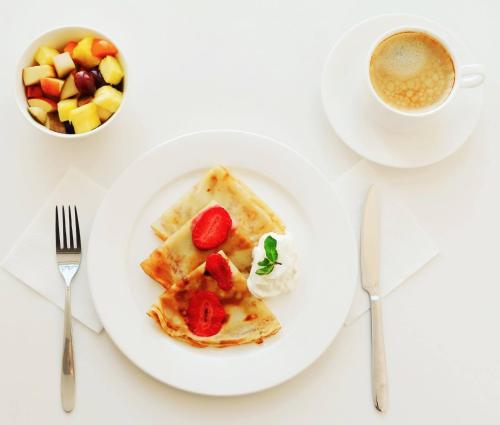 a plate of waffles with strawberries and a cup of coffee at Anastasia Mini-Hotel in Saint Petersburg