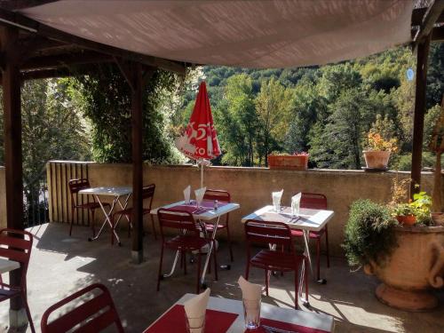 un patio con mesas, sillas y una sombrilla roja en Auberge de Barnas en Barnas