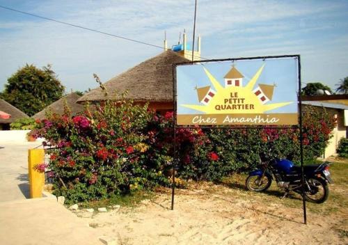a sign for a hotel with a motorcycle parked in front at Le Petit Quartier "Chez Amanthia" in Cap Skirring