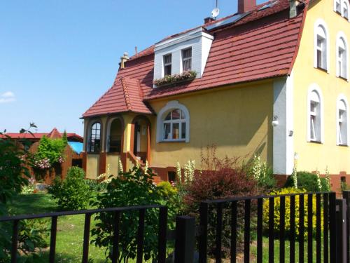 a yellow house with a red roof and a fence at Góściniec Iwona in Głuchołazy