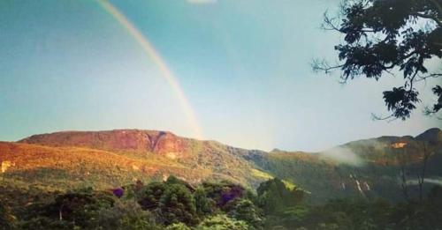 a rainbow in the sky over a hill with trees at Chalé Solar no Matutu in Aiuruoca