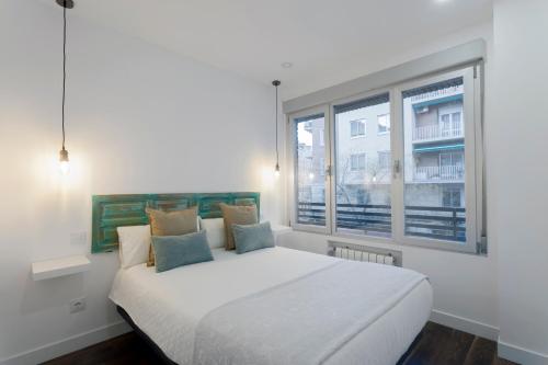 Cama blanca en habitación con ventana en dobohomes - Fernando el Católico en Madrid