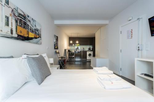 a white bedroom with a white bed and a kitchen at FLH Studio Alfama in Lisbon