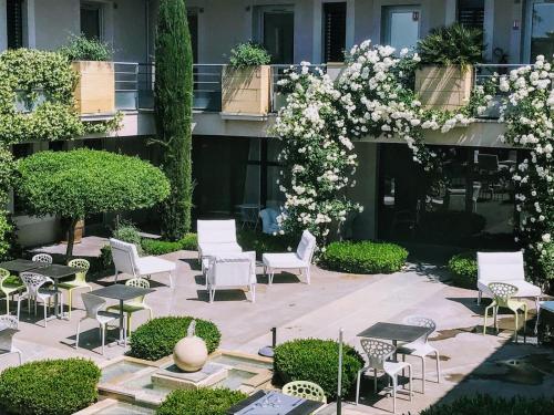 une cour avec des chaises blanches, des tables et des fleurs dans l'établissement Patio De Violette, à Uzès