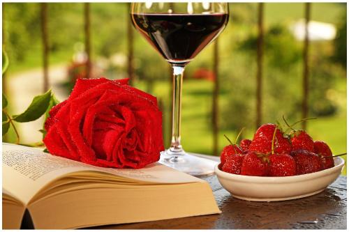 a glass of wine and a bowl of strawberries and a book at Amalia Cascina in Langa in Monforte dʼAlba