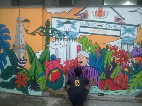 a person standing in front of a wall with a mural at Home Addicts Hostel in Yogyakarta