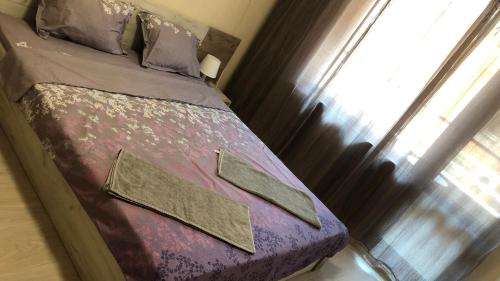 Elle comprend un petit lit avec des draps violets et une fenêtre. dans l'établissement Beach Apartments Pomorie, à Pomorie