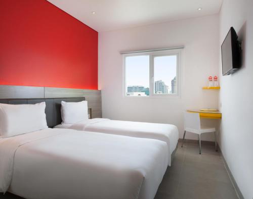 two beds in a room with a red wall at Amaris Hotel Mangga Besar in Jakarta