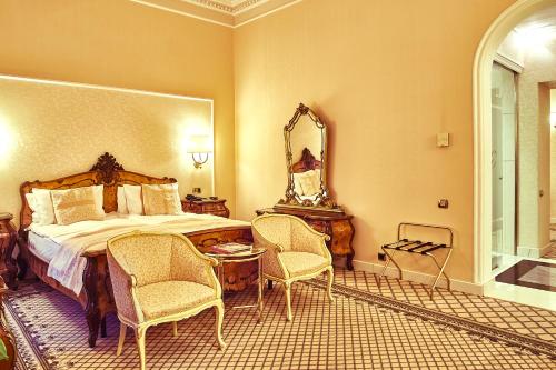 a bedroom with a bed and two chairs and a mirror at Grand Hotel Continental Bucuresti in Bucharest