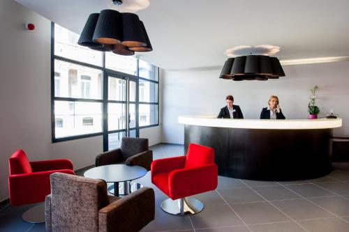 two people standing at a counter in a waiting room at Hôtel Panorama in Lourdes