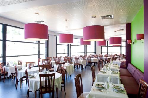 a restaurant with white tables and chairs and pink chandeliers at Hôtel Panorama in Lourdes