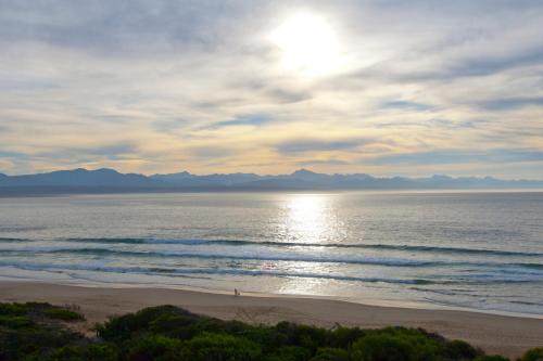 a beach with the sun shining on the water at Plett Beachfront Accommodation in Plettenberg Bay