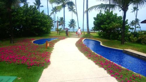 a person walking down a path next to a pool with flowers at Muro Alto Malawi Beach Dream in Porto De Galinhas