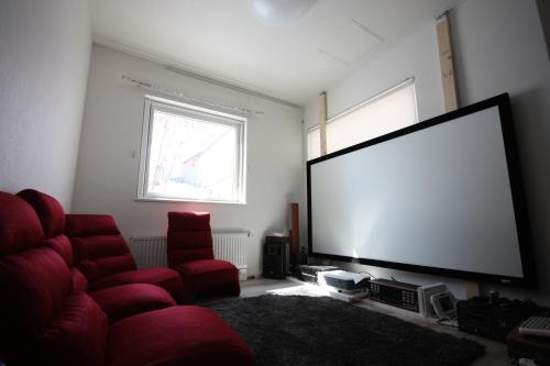 a living room with a large screen tv and red chairs at TEINE WHITE HOUSE in Sapporo